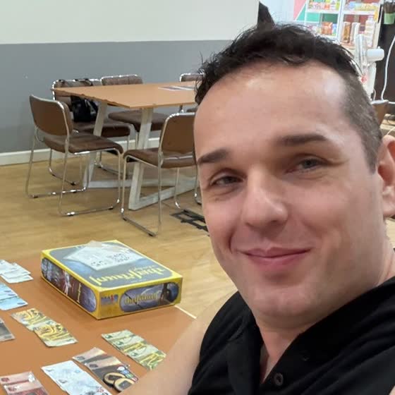 Robert Pruitt at a board-game table in Thailand, the Splendor cards and box laid out behind him